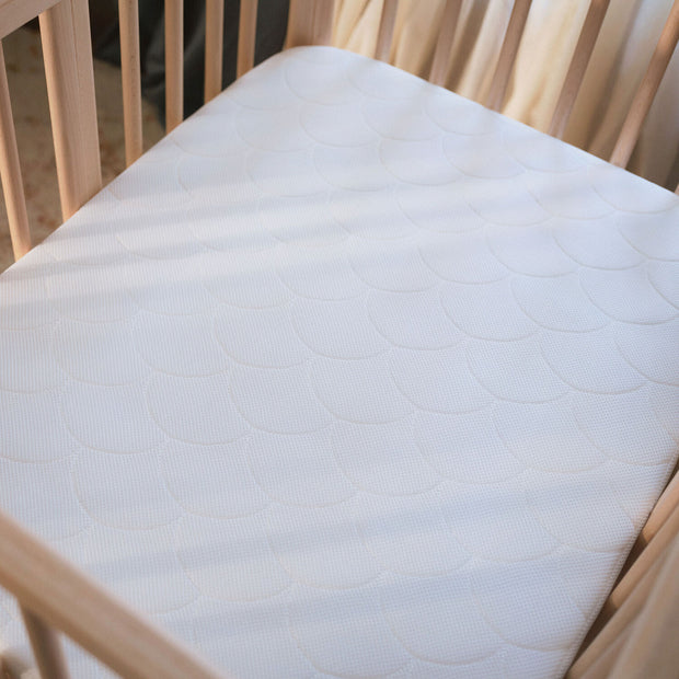 Top view of the breathable 3D mesh Stokke Nighti Bed Mattress fitted inside the Stokke Nighti natural wooden crib — Available from Parent Studio