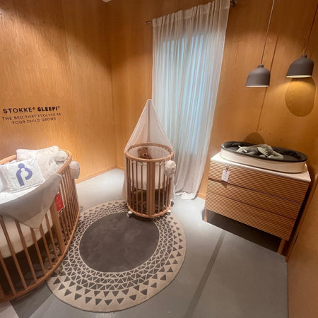 Stokke Sleepi Nursery room with wooden crib, bassinet, and dresser against a wooden wall.