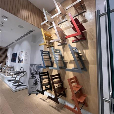 Colorful wall-mounted Stokke Tripp Trapp chairs displayed in a showroom setting.