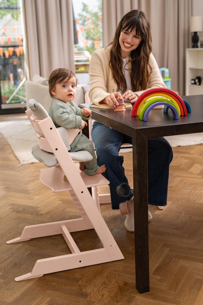 Woman and child at a dining table with a pink high chair and colorful toys.